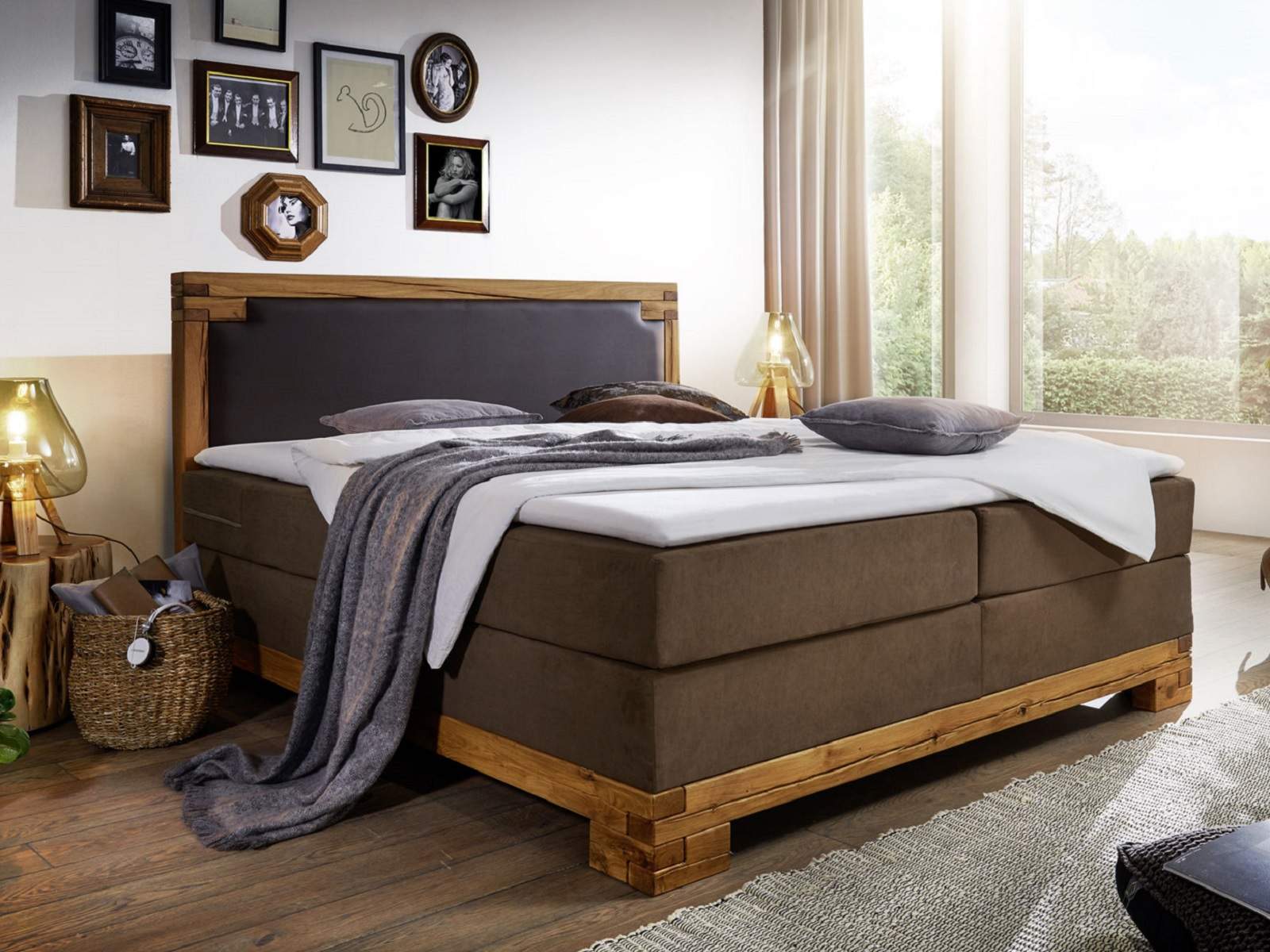Boxspringbett mit Holzrahmen und Holzfüßen in modernem Schlafzimmer, graues Kopfteil und dezente Bettwäsche, warmes Ambiente