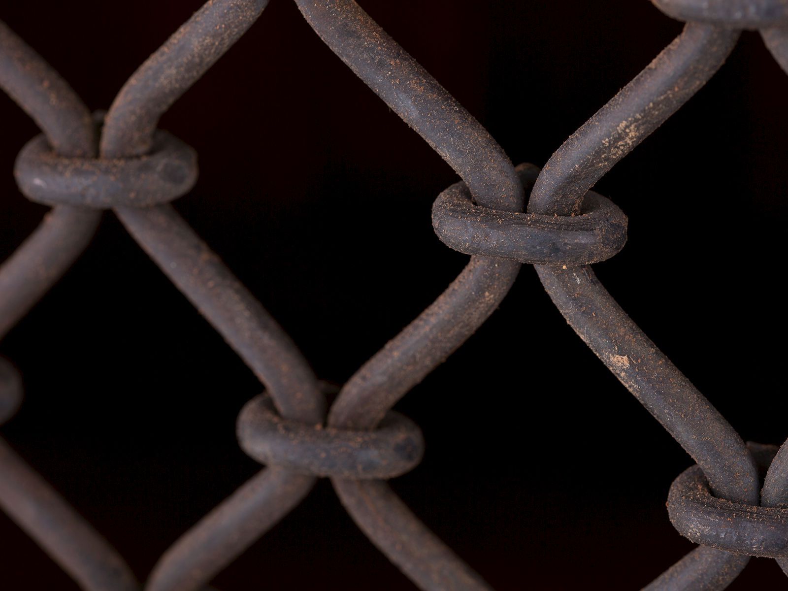 Detailbild eines rostigen Drahtgitterzauns im Diamantmuster vor dunklem, schwarzem Hintergrund. Detailbild eines rostigen Drahtgitterzauns im Diamantmuster vor dunklem, schwarzem Hintergrund.