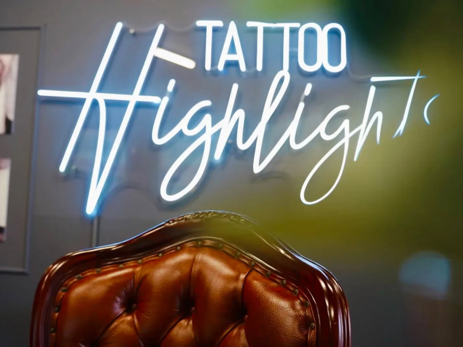 Brauner Ledersessel mit gepolsterter Rückenlehne vor dem leuchtenden Schriftzug „Tattoo Highlights“ an einer dunkelgrauen Wand.