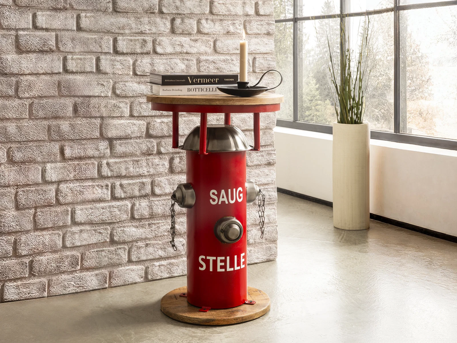Roter Beistelltisch im Hydranten-Design mit Holzplatte, Aufschrift „SAUG STELLE“, dekoriert vor Backsteinwand und Fensterfront
