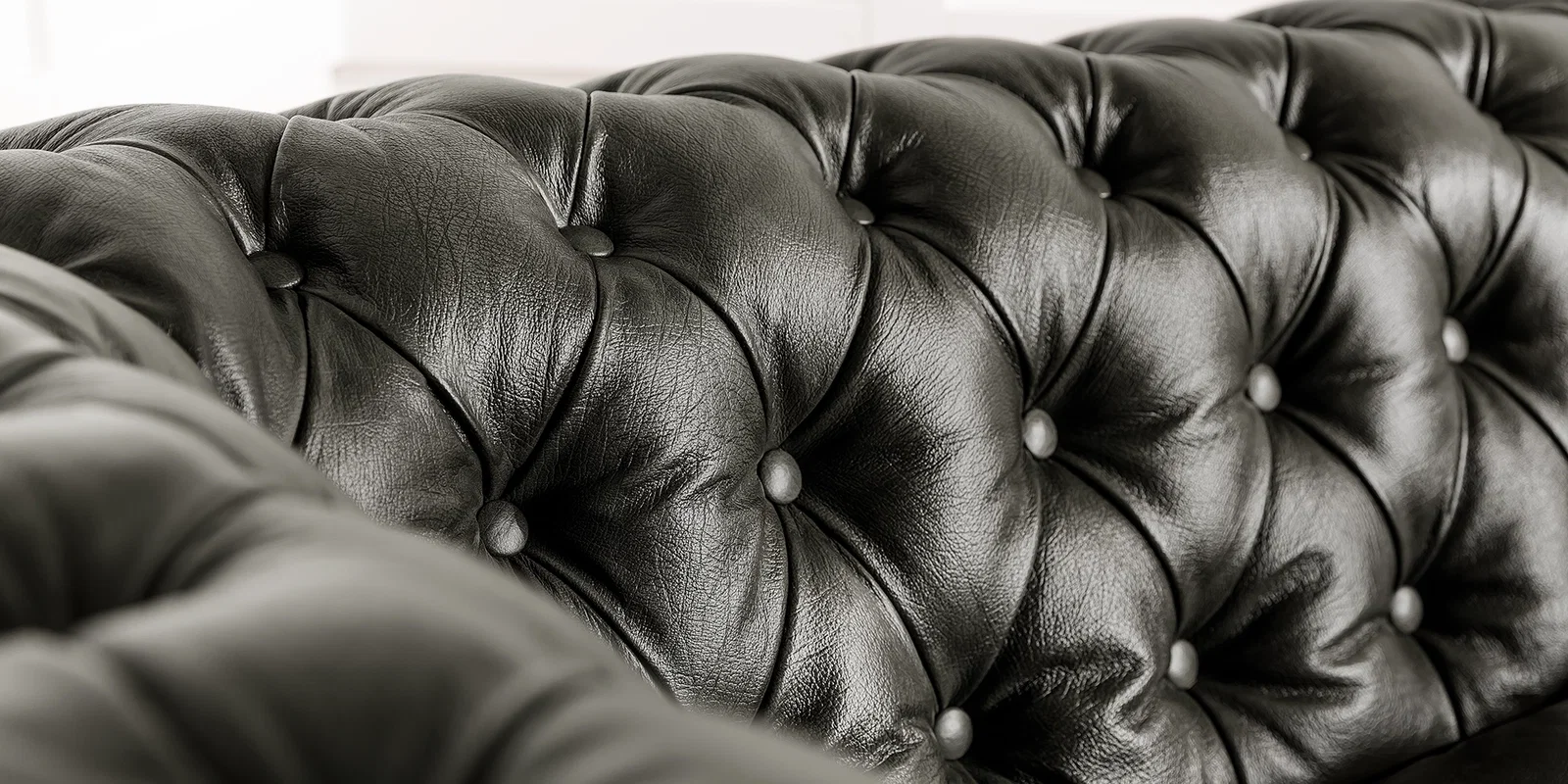 Chesterfield-Detail: Nahaufnahme typischer Knopfheftung, gerollter Armlehne und genarbter Lederoberfläche