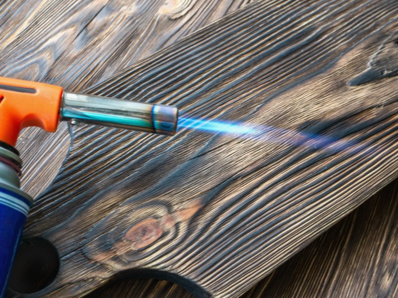 Upcycling-Holz beim Abflammen: Flamme an Holzbretträndern, schwarz-braune angekohlte Oberfläche, texturreiches Detail