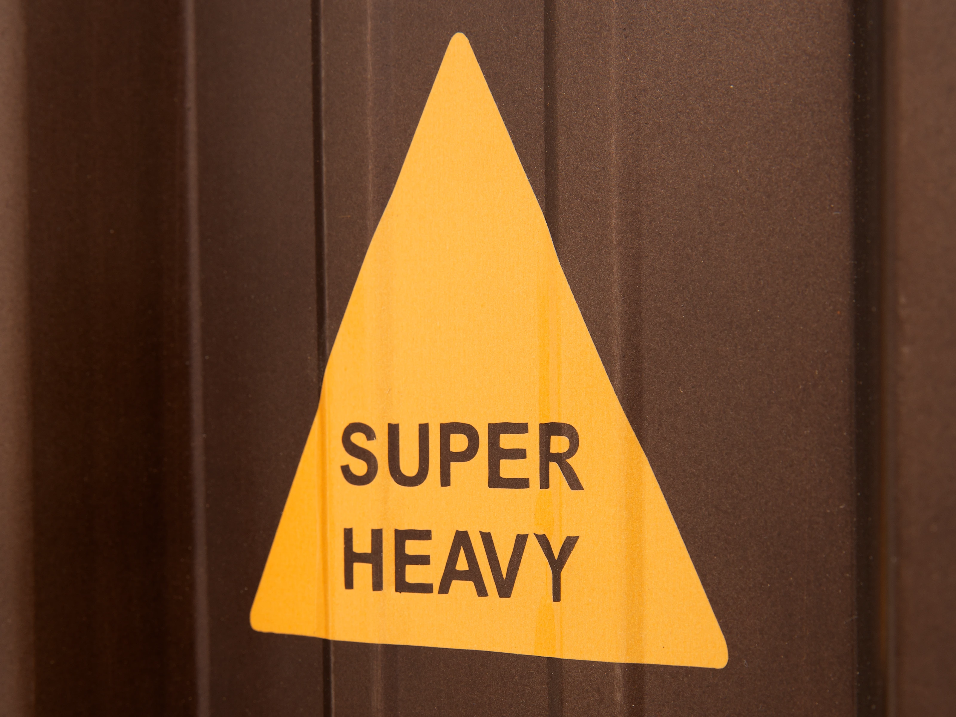 Detailbild des Warnhinweises „Super Heavy“ auf brauner, lackierter Metallfläche – Hinweis auf hohes Gewicht der TV-Bank Cargon