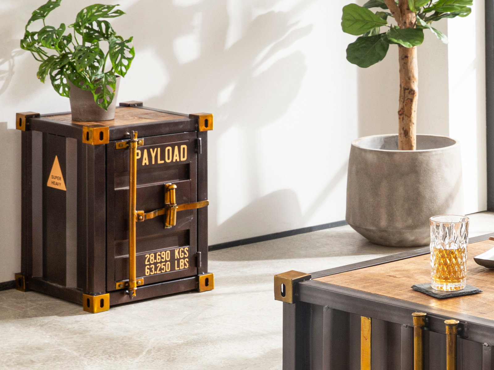 Container-Nachttisch im Industrial-Stil mit Aufdruck „Payload“, dunklem Metall, Holzplatte und Pflanzen im hellen Ambiente