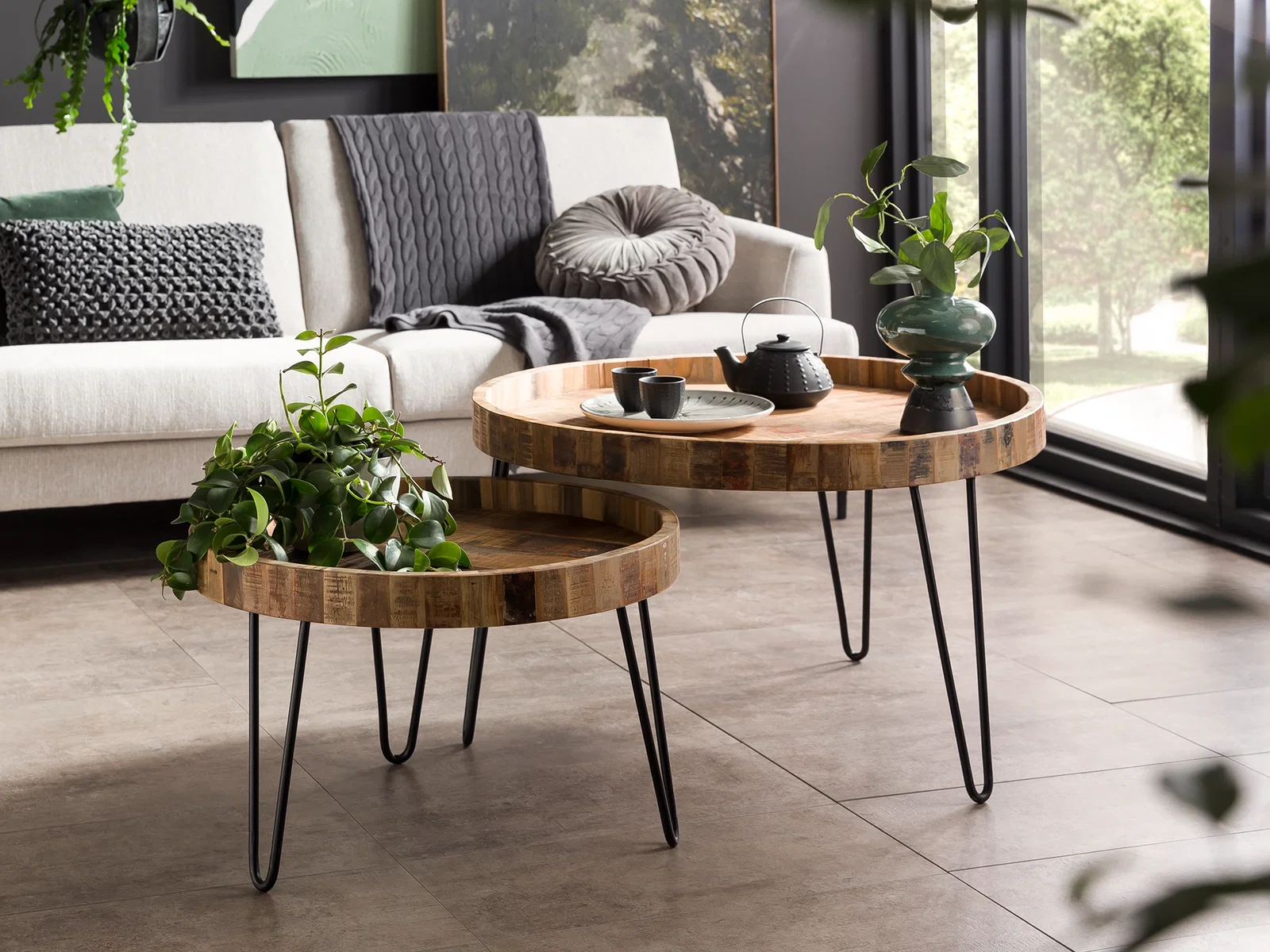 Zwei runde Couchtische der Serie Corby aus Holz und schwarzem Metall vor einem hellen Sofa