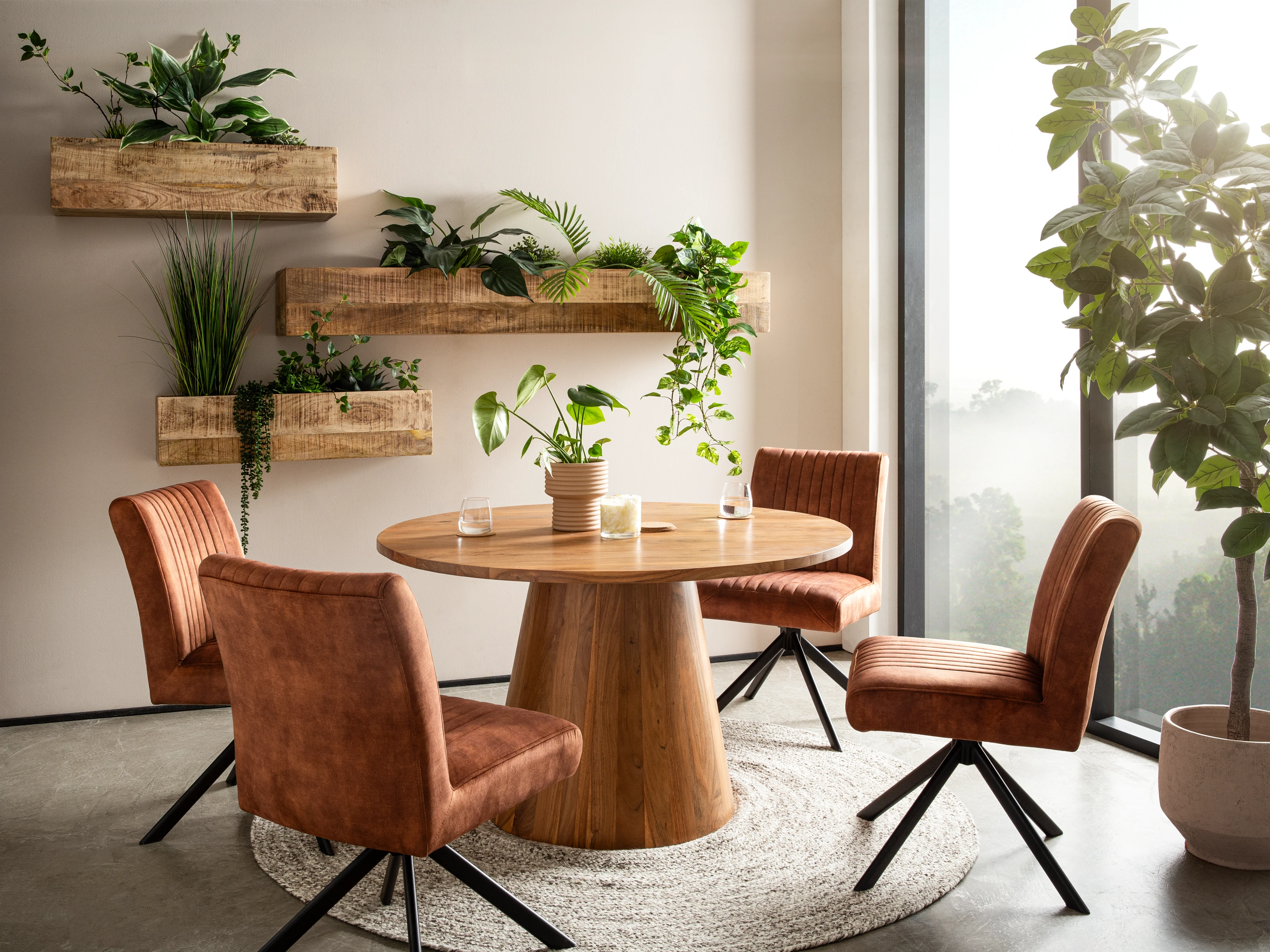 Esstisch Osbon D120cm aus lackierter Akazie, brauner Rundtisch (Ø 120×75 cm) im Wohnbeispiel mit vier Stoffstühlen und Pflanzen, 45°-Front-Seitenansicht. Wohnbeispiel: runder Massivholz-Esstisch mit 4 braunen Canton-Stühlen (45°-Ansicht) und Pflanzen-Deko