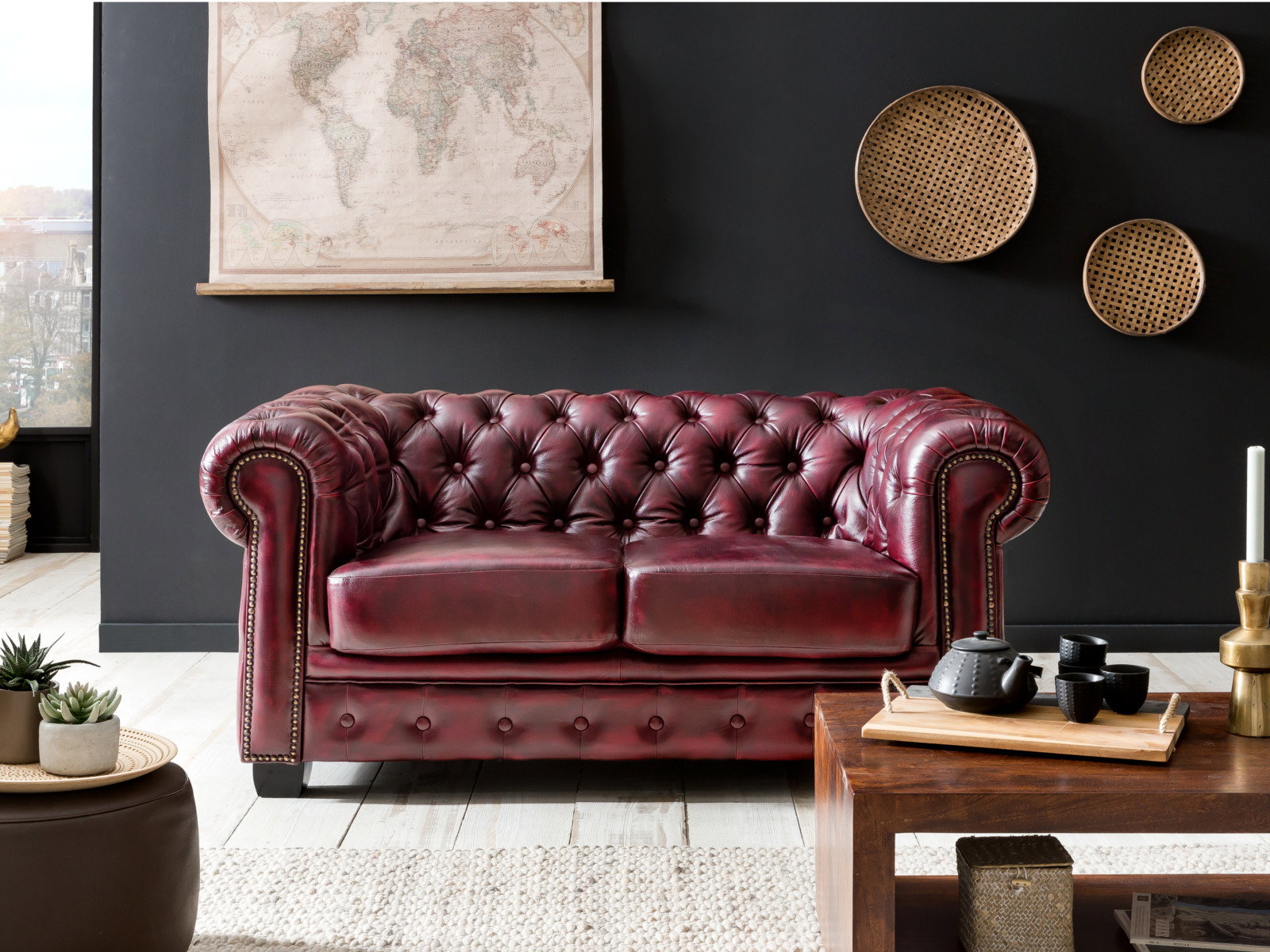 Bordeauxrotes Chesterfield Ledersofa im Vintage-Stil, 2-Sitzer in elegantem Wohnambiente mit schwarzer Wand und Holztisch