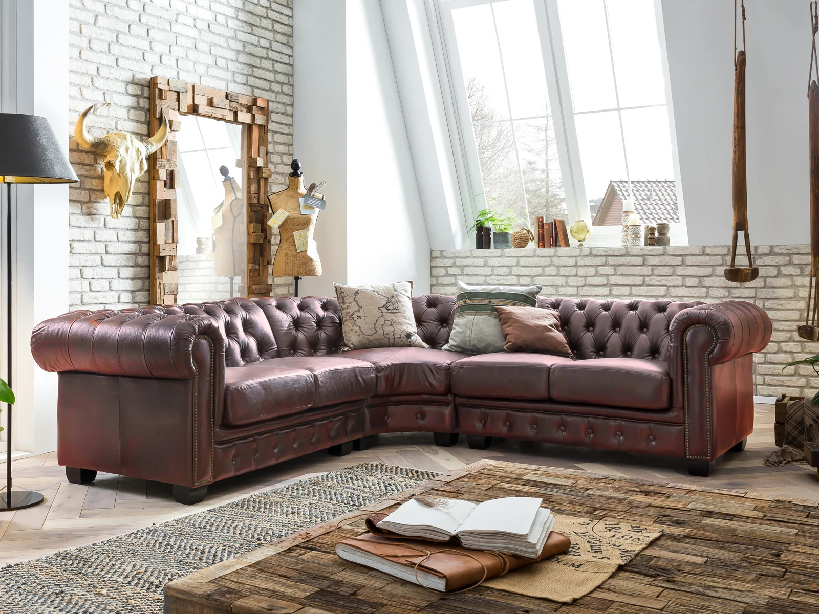 Klassisches Chesterfield-Sofa im Ambiente: tiefe Knopfheftung, gerollte Armlehnen und Holzfüße, gemütliche Wohnzimmeratmosphäre mit warmen Farben und stimmungsvoller Beleuchtung